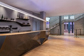 Un área de bar moderna con una barra de madera, botellas de vino en estantes y una escalera que lleva a un nivel superior.