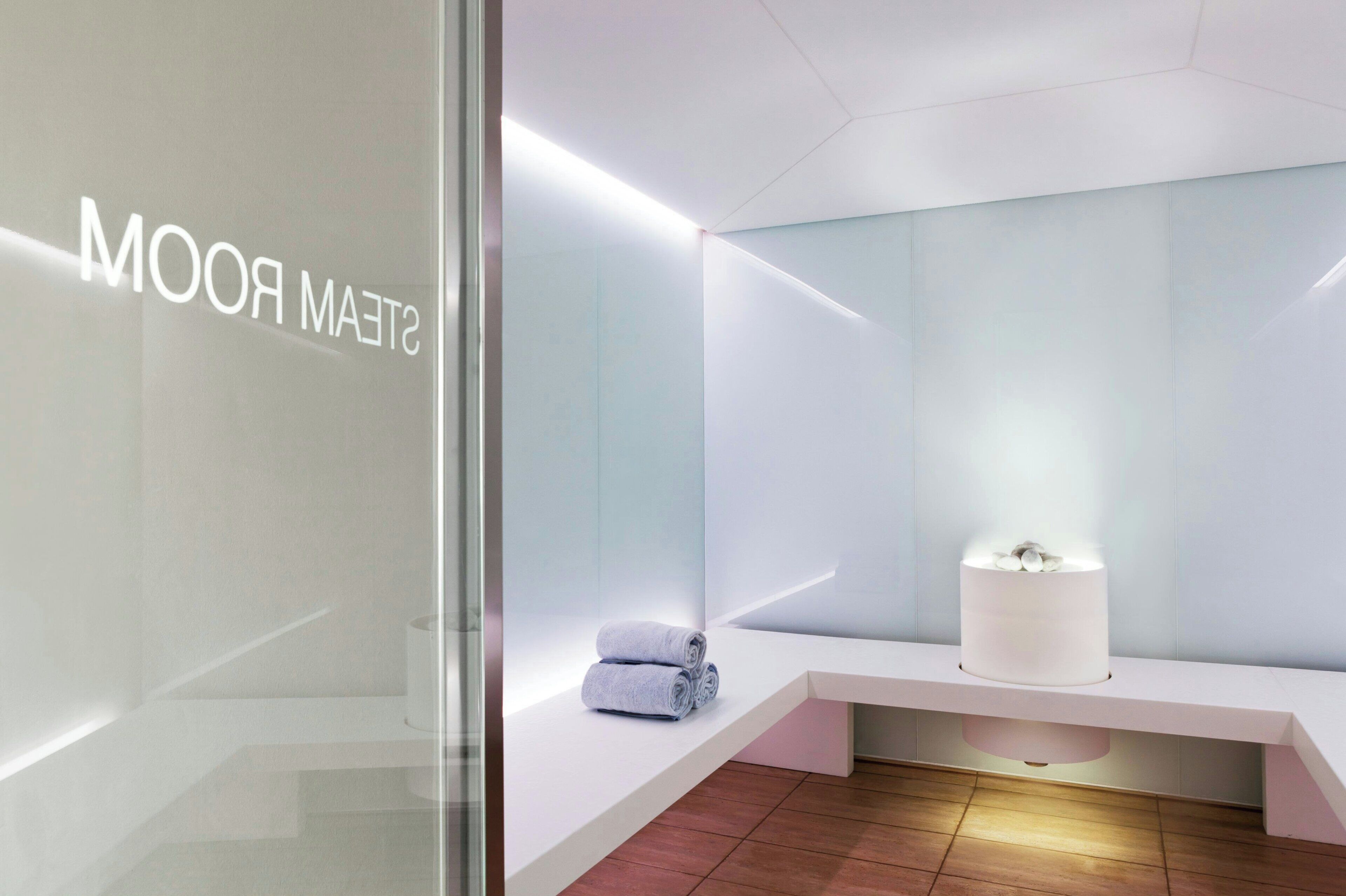 Ein modernes Badezimmer mit Glastrennwand, einer Sitzbank und einer zylindrischen Leuchte.