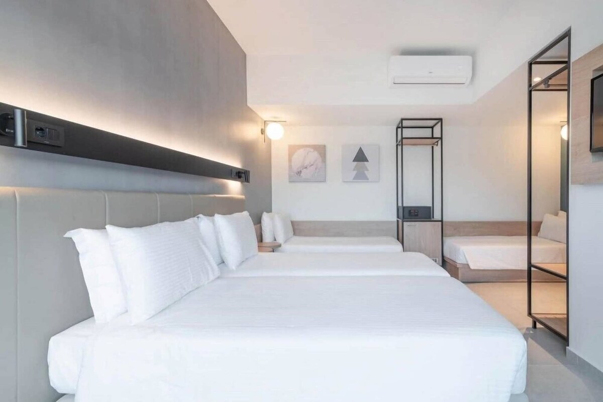 A hotel room with a large bed, bedside tables, a mirror, and a wall-mounted air conditioning unit.