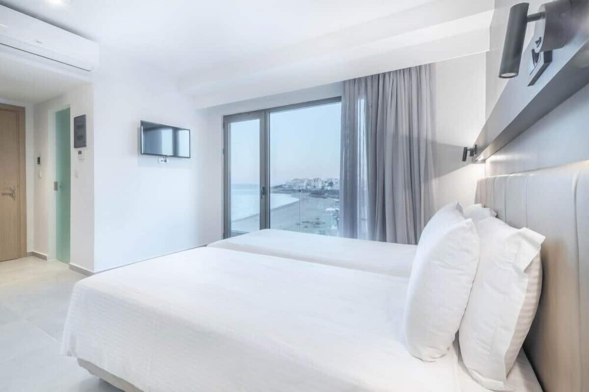 A hotel room with a large bed, a TV mounted on the wall, and a window with a view of the city.