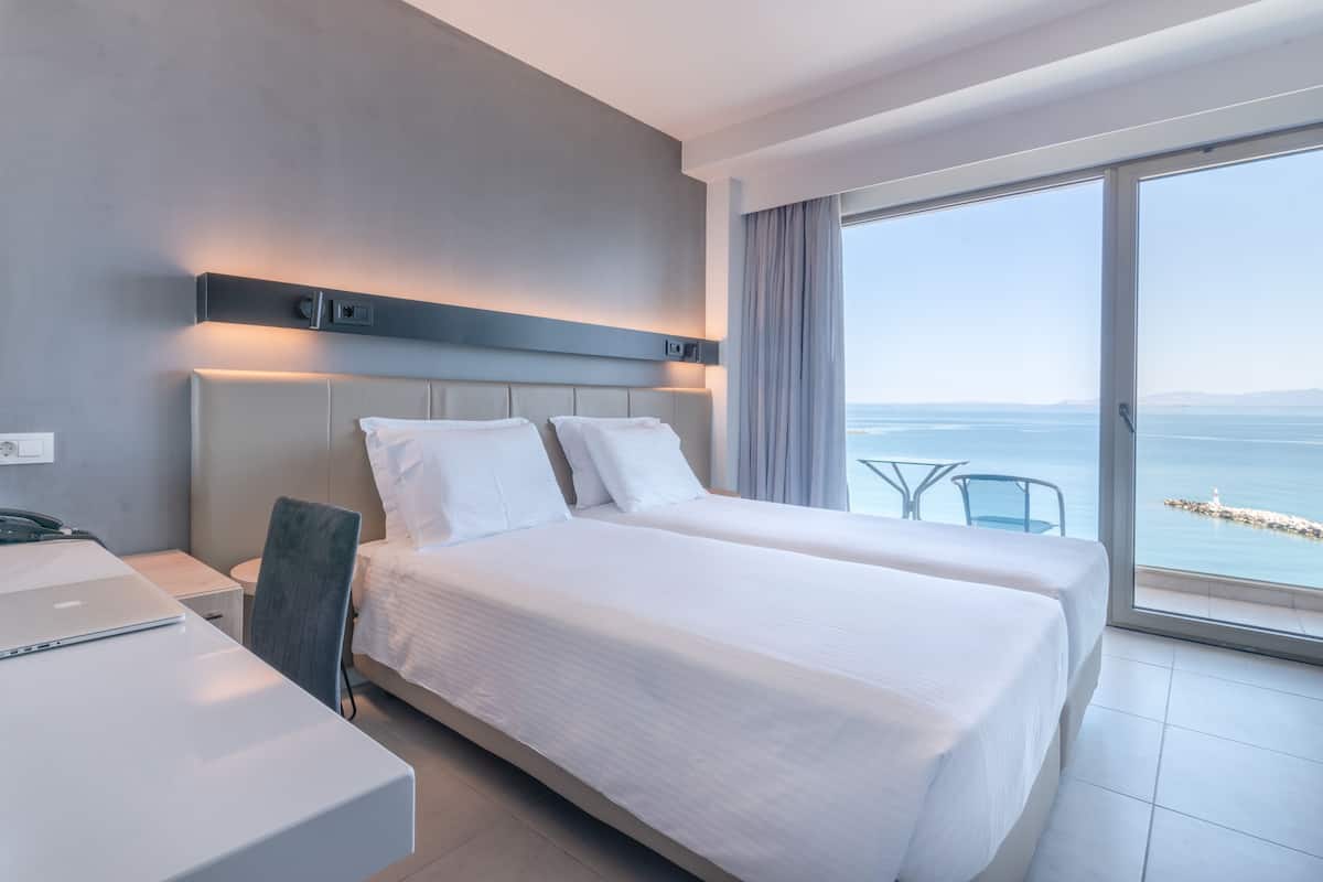 A modern hotel room with a large bed, a desk, and a view of the sea.