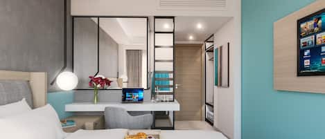 A modern hotel room with a bed, a desk with a laptop, a vase with flowers, and a breakfast tray.
