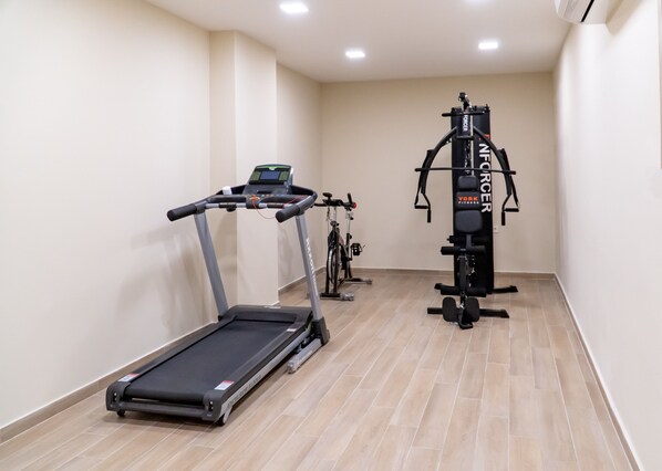 A home gym with a treadmill, stationary bike, and a multi-functional exercise machine. - Hotel Avra by Smile hotels (Rafina-Pikermi)