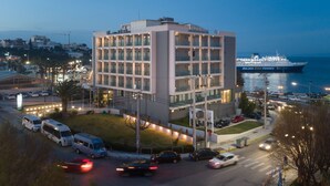 A modern hotel with a multi-story structure, a parking area, and a view of the sea.