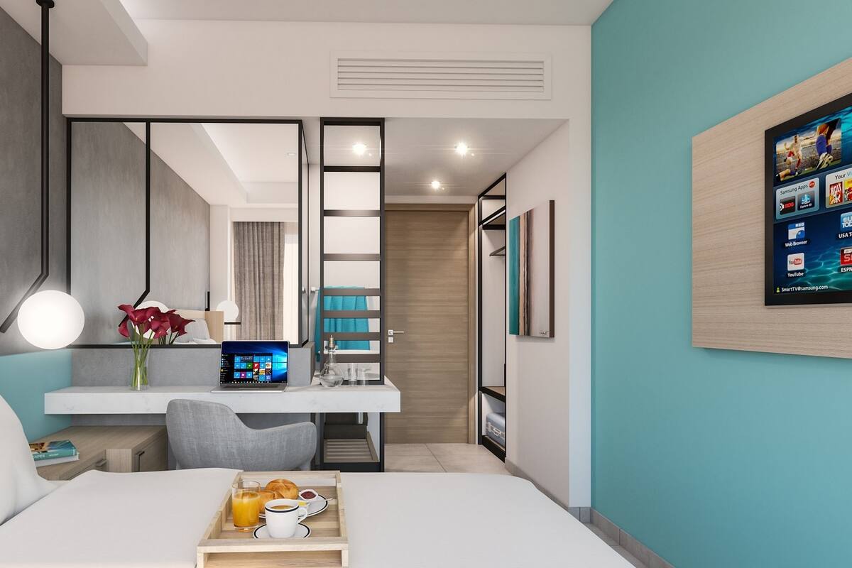 A modern hotel room with a bed, desk, and a laptop.