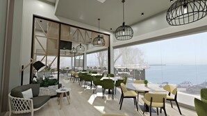 A modern dining area with high ceilings, large windows, and a view of the sea.
