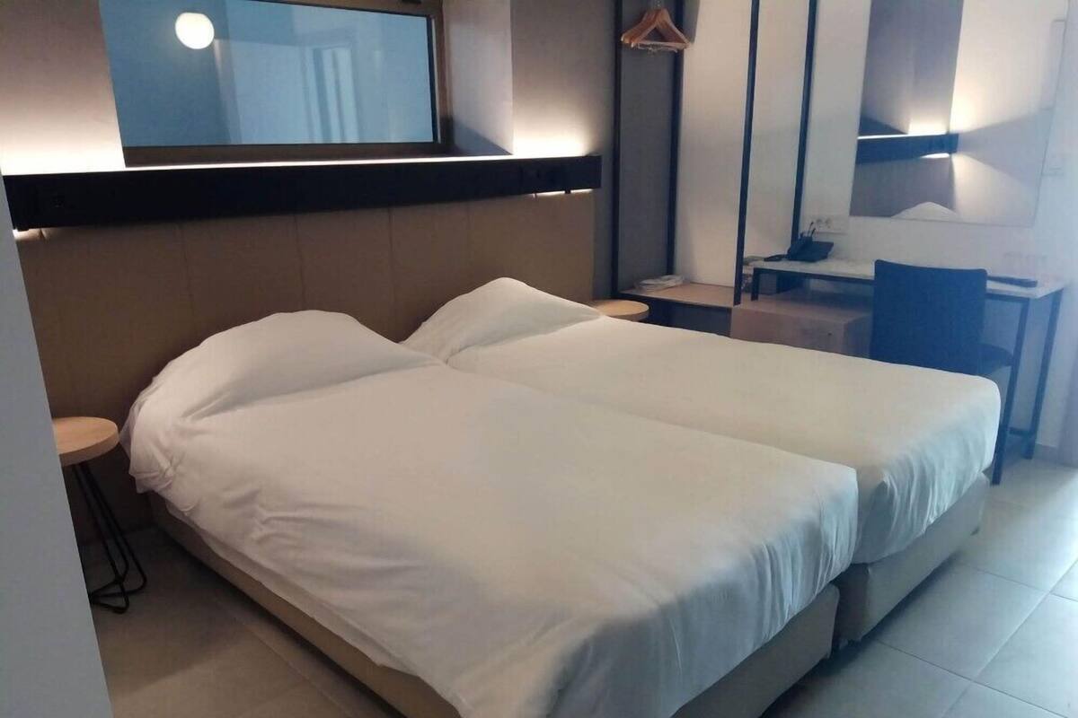 A hotel room with two beds, a desk, a chair, a mirror, and a hanging coat rack.