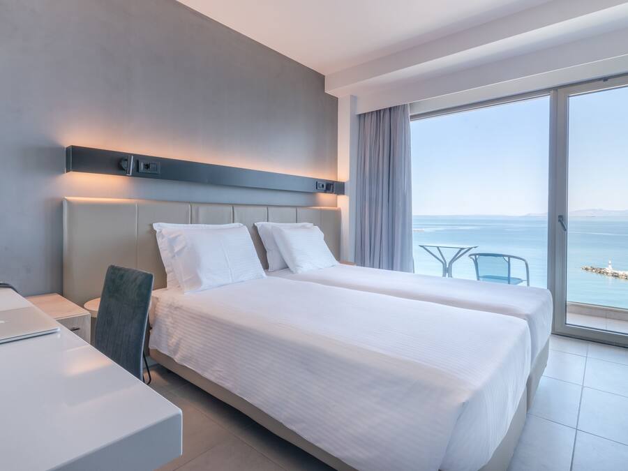 A modern hotel room with a large bed, a desk, and a view of the sea.