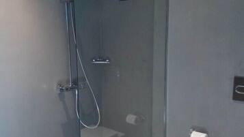 A modern bathroom with a glass-enclosed shower, a toilet, and a trash bin.