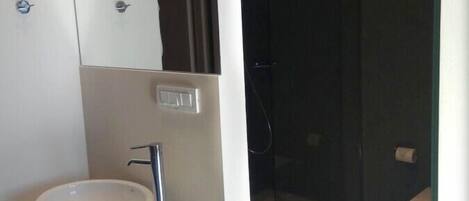 Un baño moderno con lavamanos blanco, espejo y cabina de ducha con vidrio.
