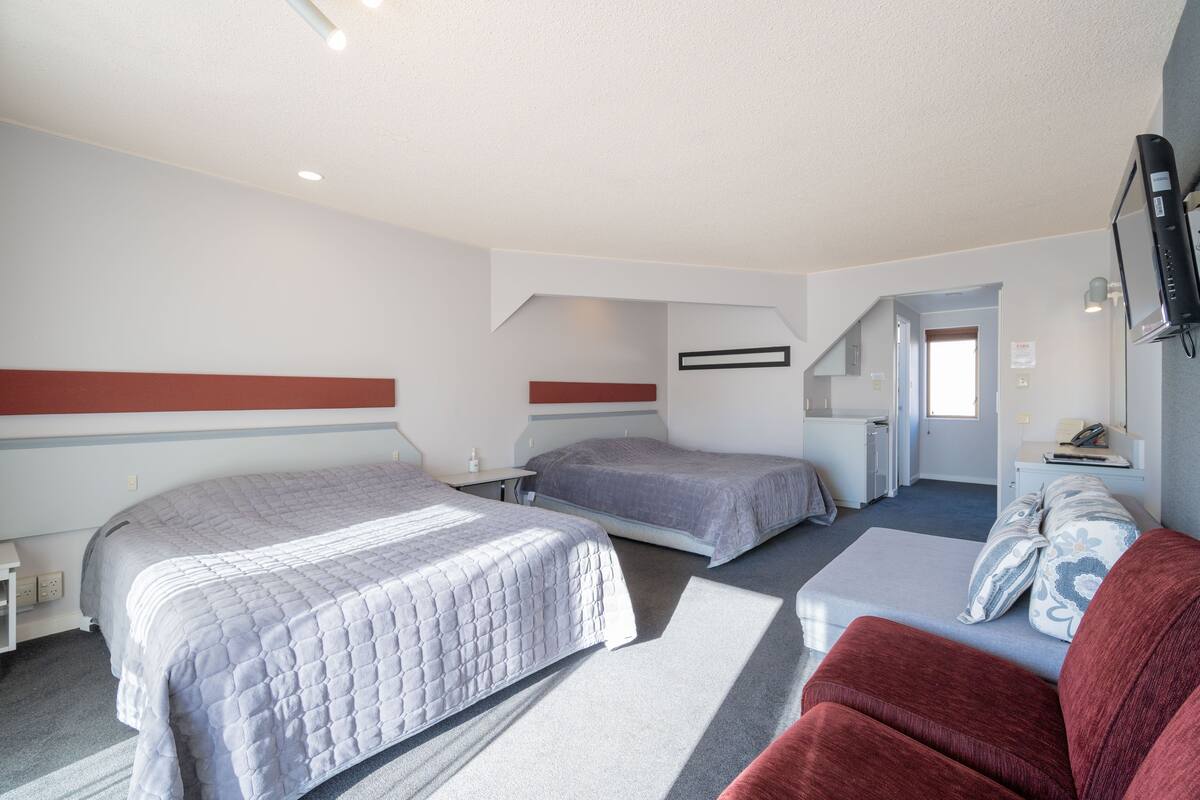Habitación de hotel con dos camas, un sofá rojo, un televisor y una kitchenette.