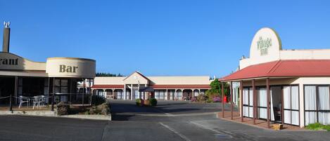 Un edificio con un letrero que dice 'Bar' y otro que dice 'Village Inn', con un área de asientos al aire libre cubierta y un estacionamiento.