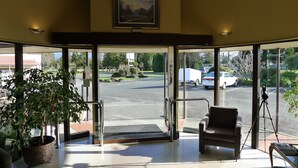 Un hall d’hôtel avec une grande porte vitrée, une plante en pot, un fauteuil en cuir et un trépied à l’extérieur.