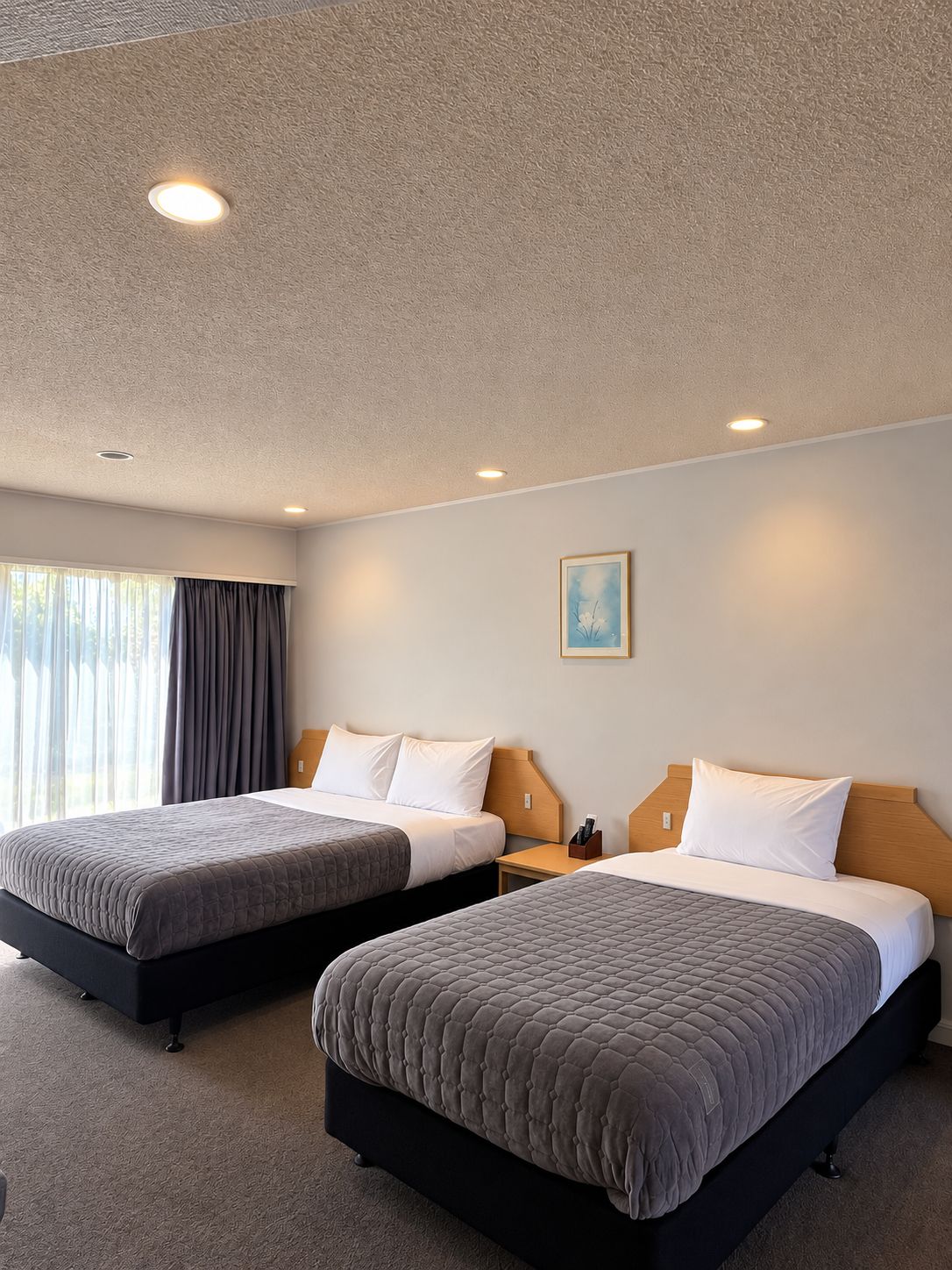 Ein Hotelzimmer mit zwei Betten, einem Bild an der Wand und einem Fenster mit Vorhängen.