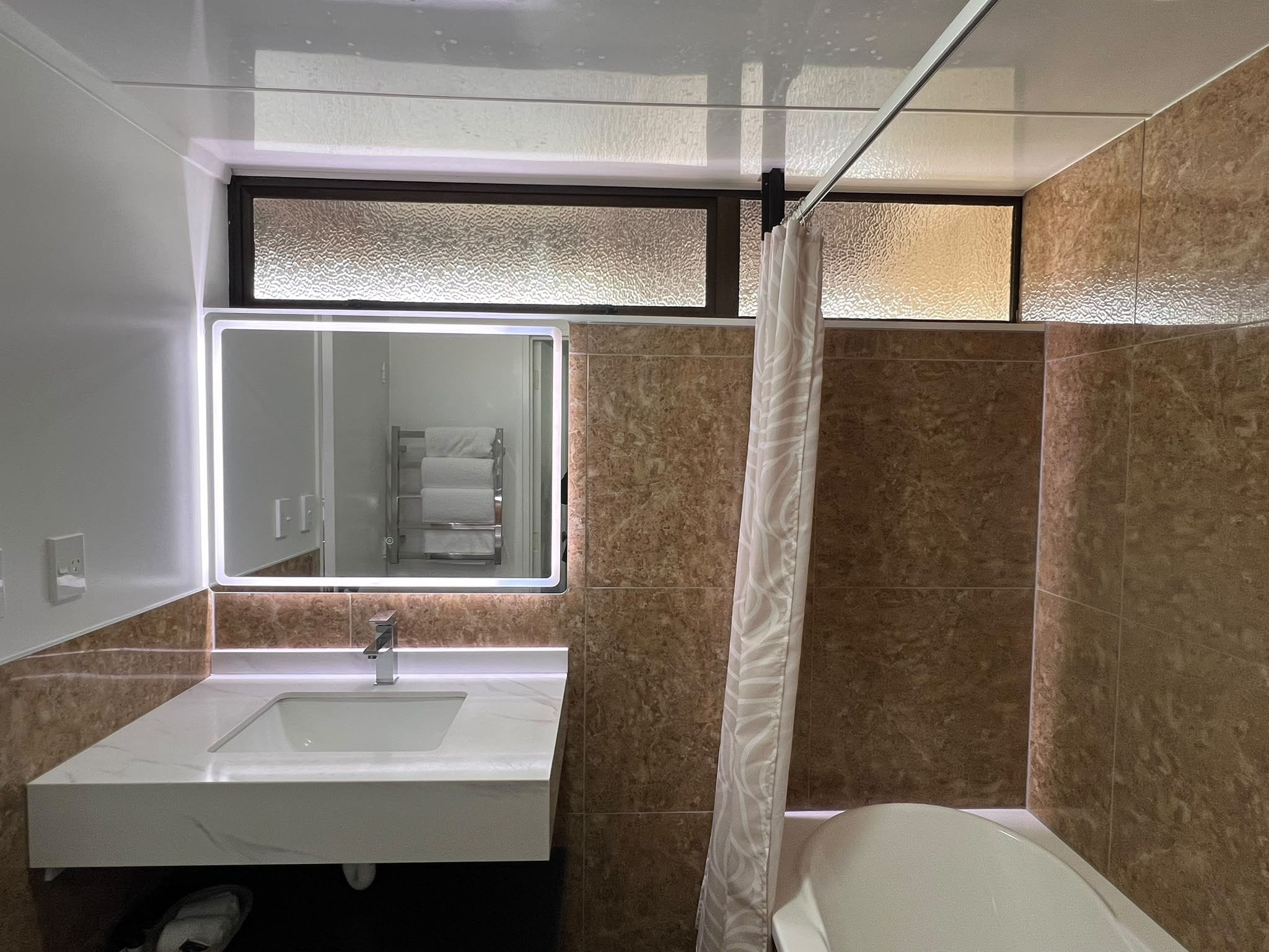 A modern bathroom with a large mirror, a sink, and a shower area.