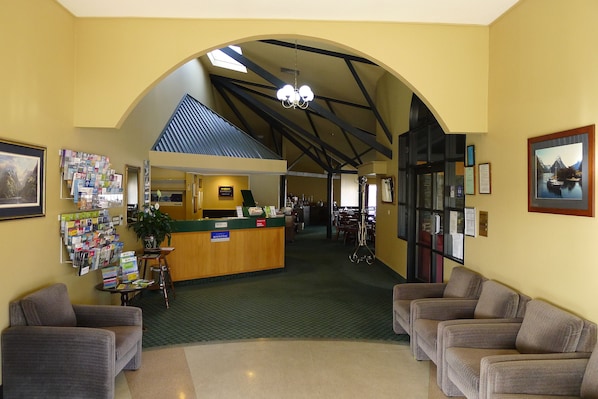 A reception area with a counter, seating, and a view of the dining area. - The Village Inn Hotel (Te Anau)