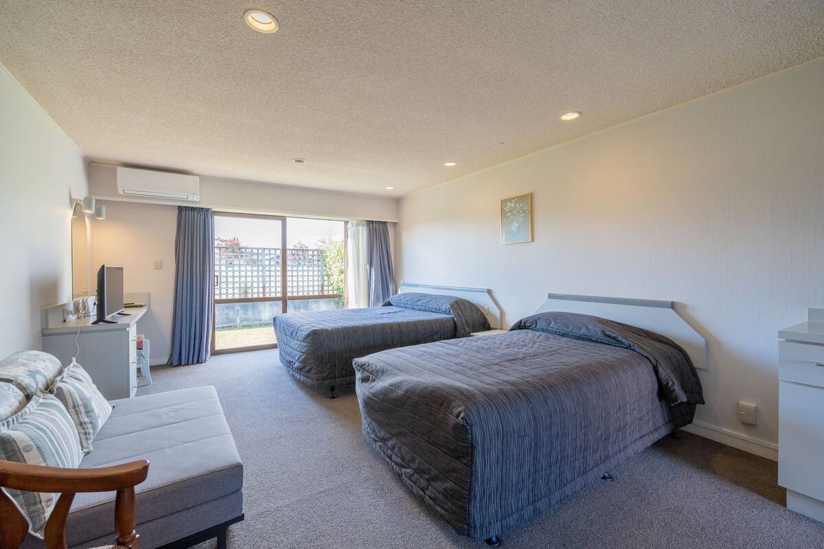 Habitación de hotel con dos camas, un escritorio, una silla y un ventanal grande.