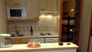 A kitchen with a microwave, stove, and sink. There is a dining table with plates, bowls, and a pitcher of orange juice. - Résidence Val Claret (Tignes)