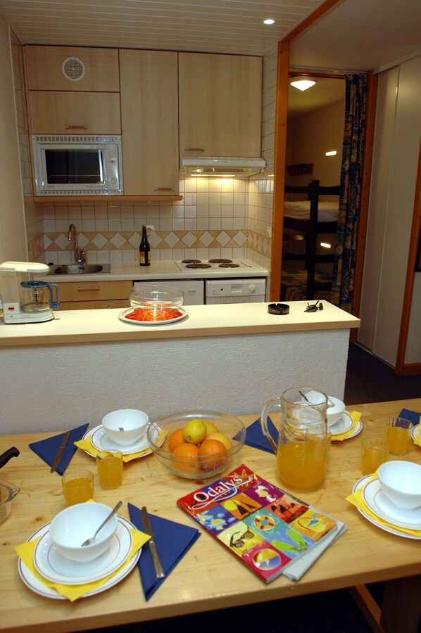 A kitchen with a microwave, stove, and sink. There is a dining table with plates, bowls, and a pitcher of orange juice.