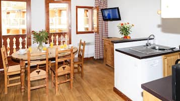A kitchen with wooden cabinets, a dining table with chairs, a TV mounted above the sink, and a window with a view of balconies.
