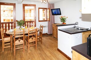A kitchen with wooden cabinets, a dining table with chairs, a TV mounted above the sink, and a window with a view of balconies. - Résidence Val Claret (Tignes)
