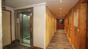 A corridor with wooden paneling, a glass elevator, and a wooden floor. - Résidence Val Claret (Tignes)