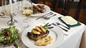A dining table set with plates of food, glasses, and cutlery, a candle, and a fireplace in the background. - Cameron Estate Inn & Restaurant (Mount Joy)