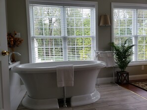 A bathroom with a freestanding bathtub, a sink, a mirror, and a window with blinds.