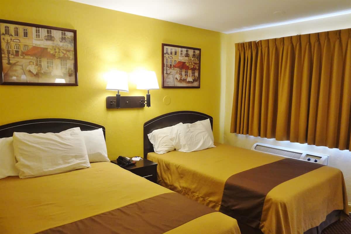 A hotel room with two beds, yellow walls, and two paintings.