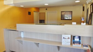 A reception desk with a light wood finish, a clock above it, and a framed picture on the wall. - Americas Best Value Inn Goldsboro (Goldsboro)