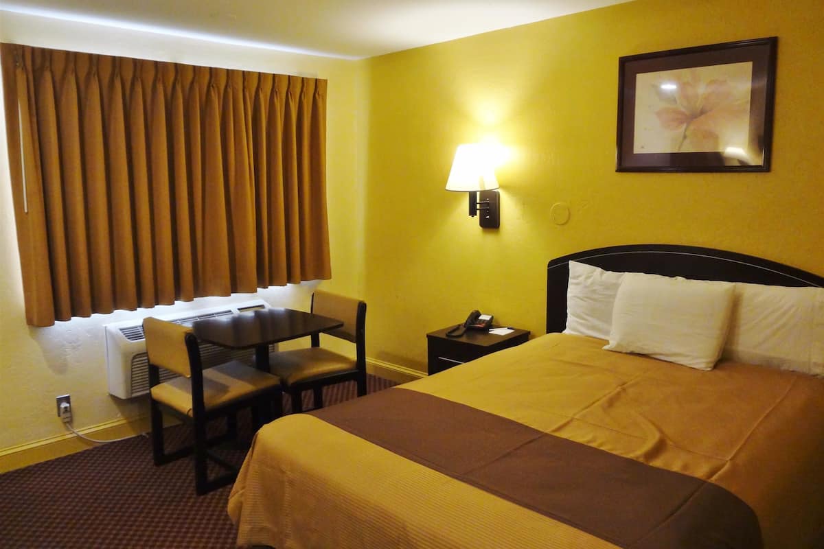 A hotel room with a bed, a desk, a chair, a lamp, and a picture on the wall.