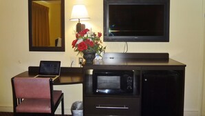 A hotel room with a desk, a laptop, a microwave, a TV, a mirror, and a vase with flowers. - Americas Best Value Inn Goldsboro (Goldsboro)