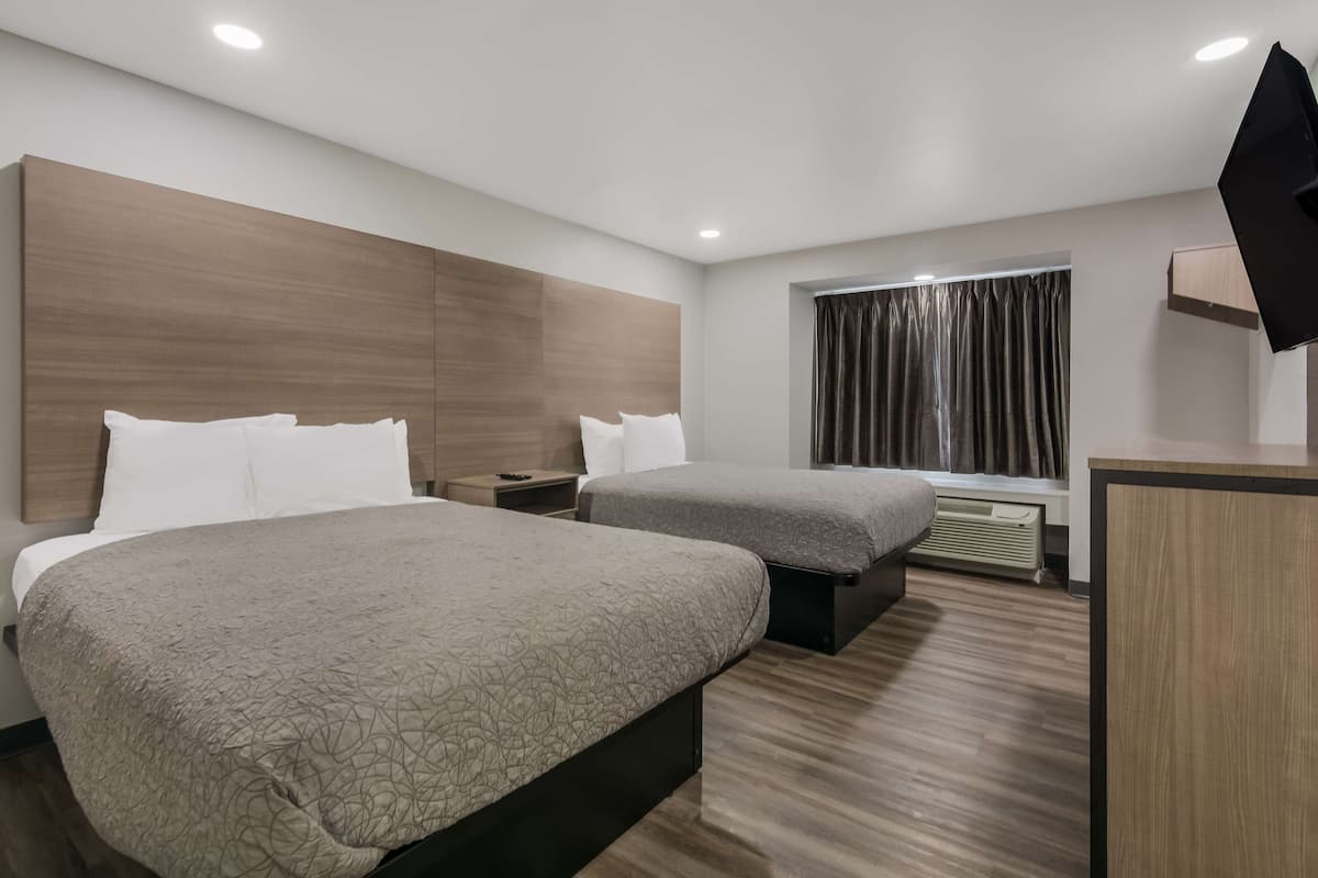 A modern hotel room with two beds, a desk, a flat-screen TV, and a window with curtains.