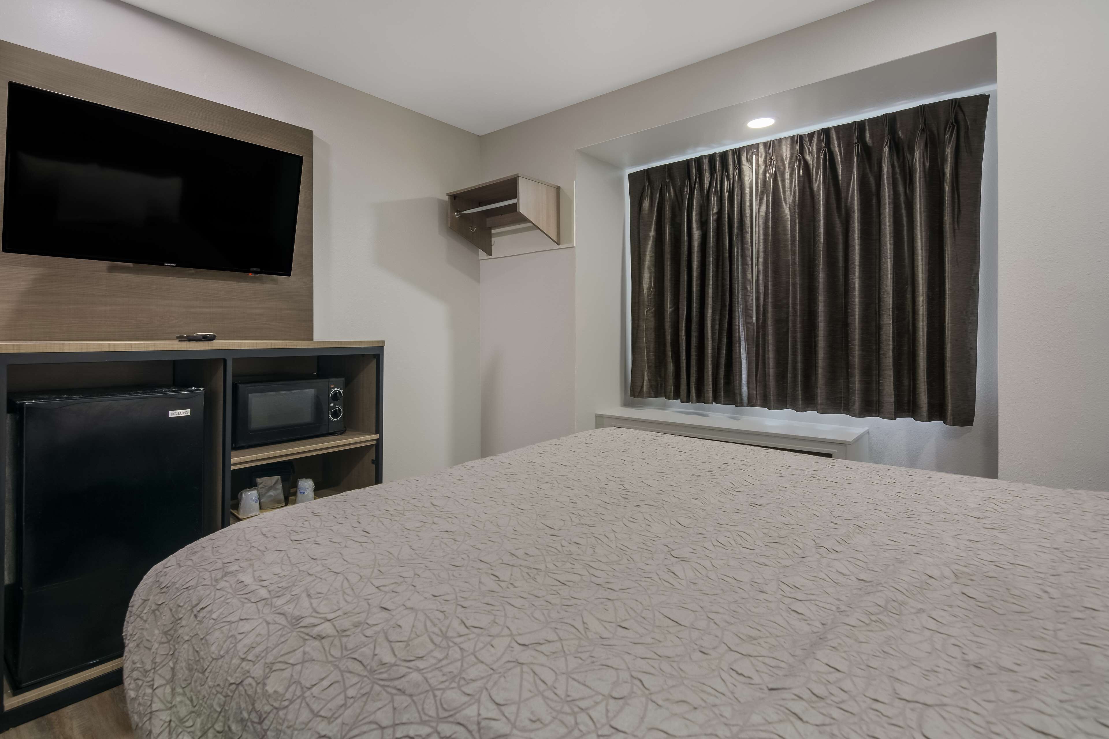 Habitación de hotel con cama, televisor montado en la pared, microondas y refrigerador.
