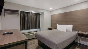 Una habitación de hotel moderna con una cama, un escritorio, un ventanal con cortinas, una mesita de noche y un aire acondicionado instalado en la pared.