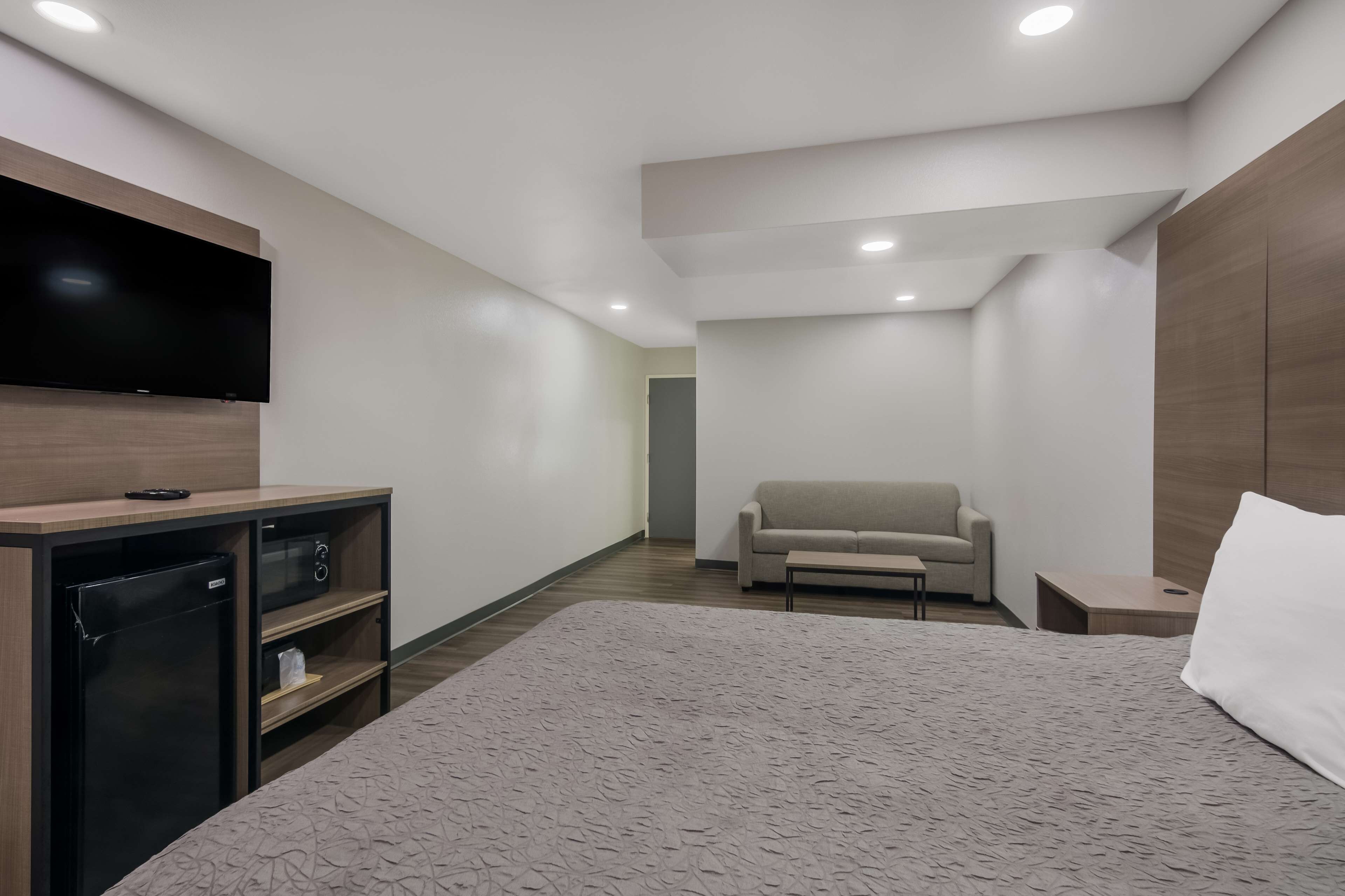 Una camera d'albergo moderna con un letto grande, una TV a schermo piatto montata su un mobile in legno, un divano e un tavolino.