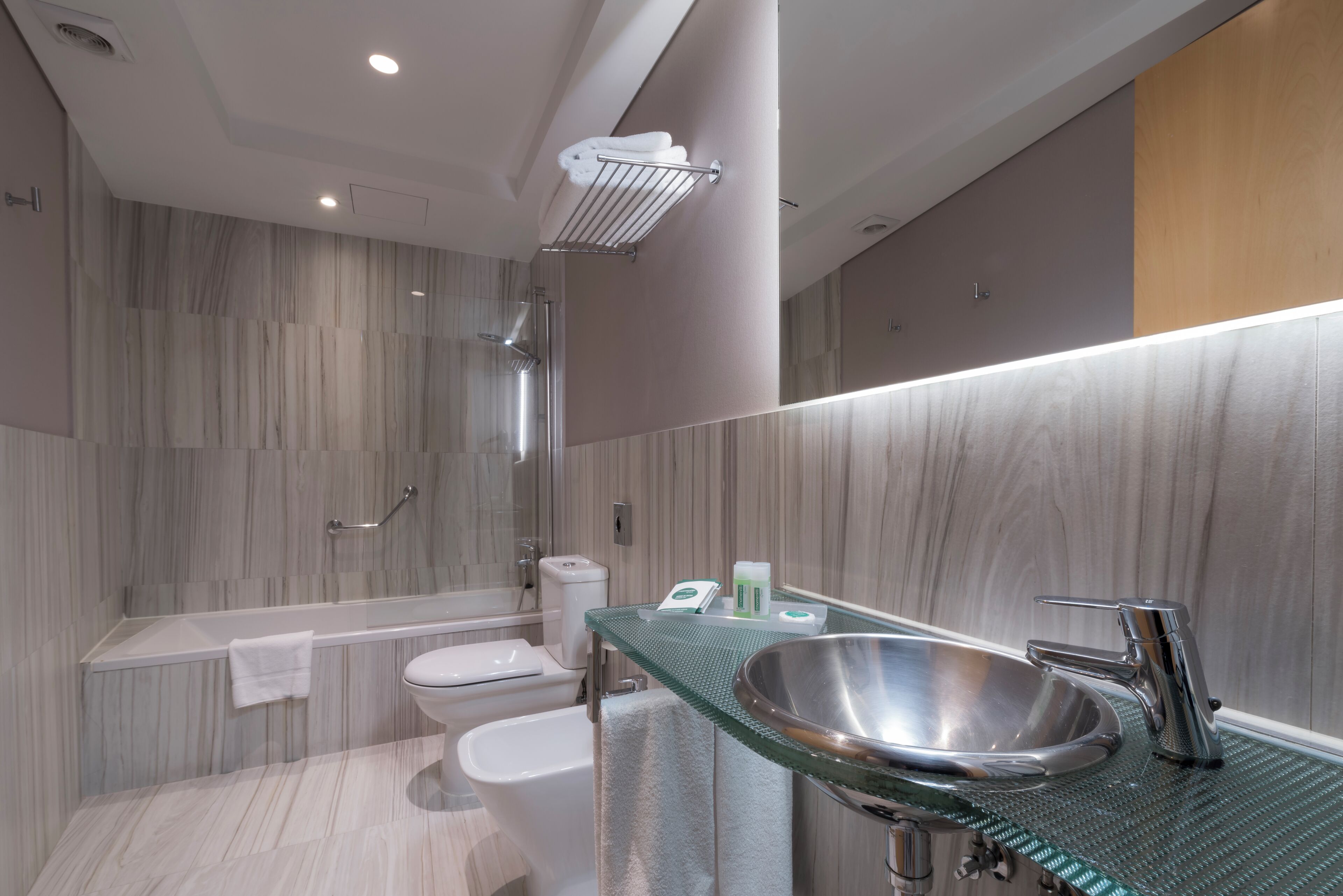 A modern bathroom with a glass countertop sink, a shower, and a toilet.