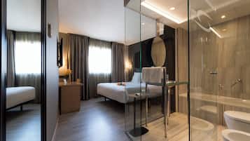 Una habitación de hotel moderna con ducha de vidrio, una cama con mesita de noche y un espejo grande.