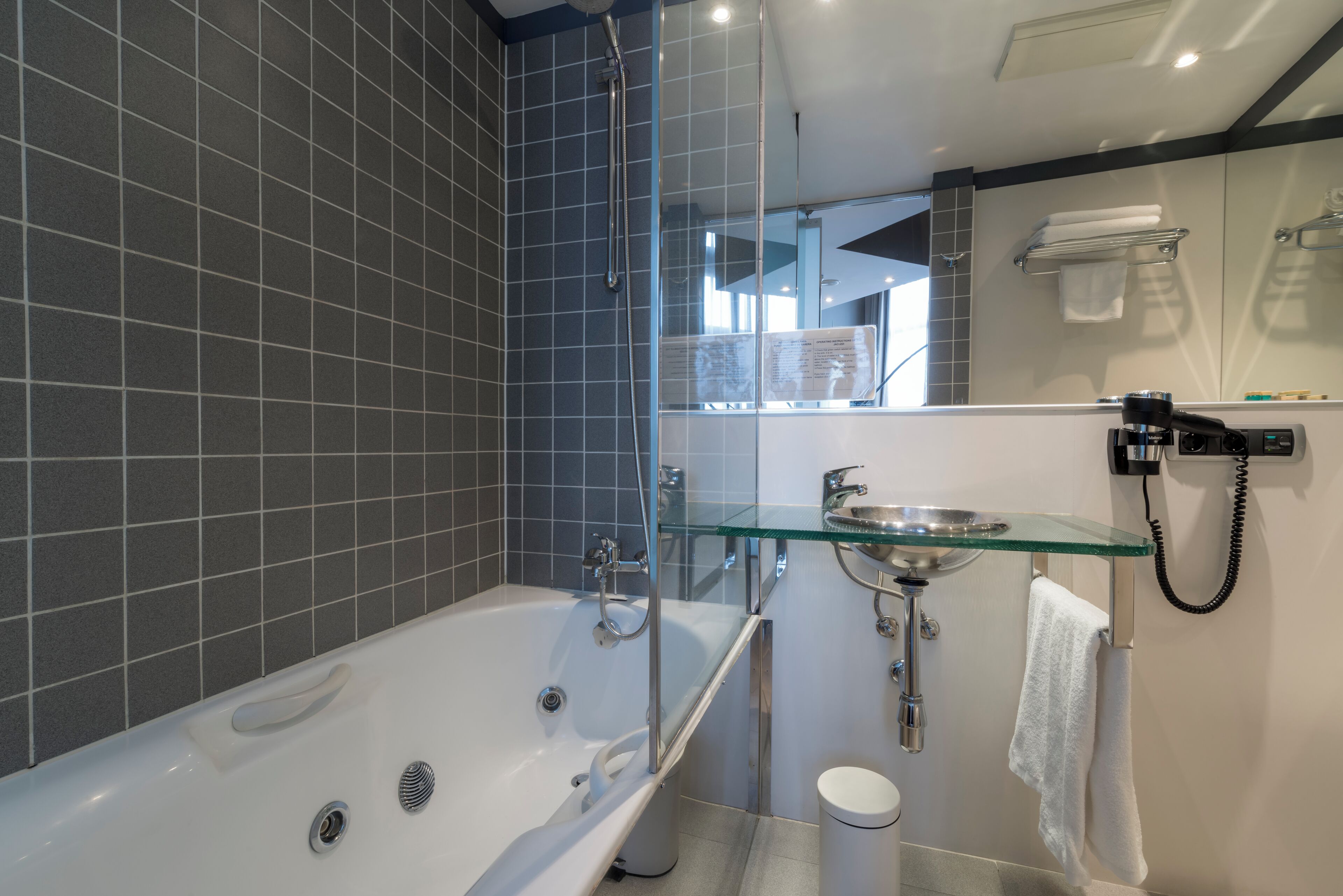 Un baño moderno con bañera vidriada, lavamanos de cristal y espejo.