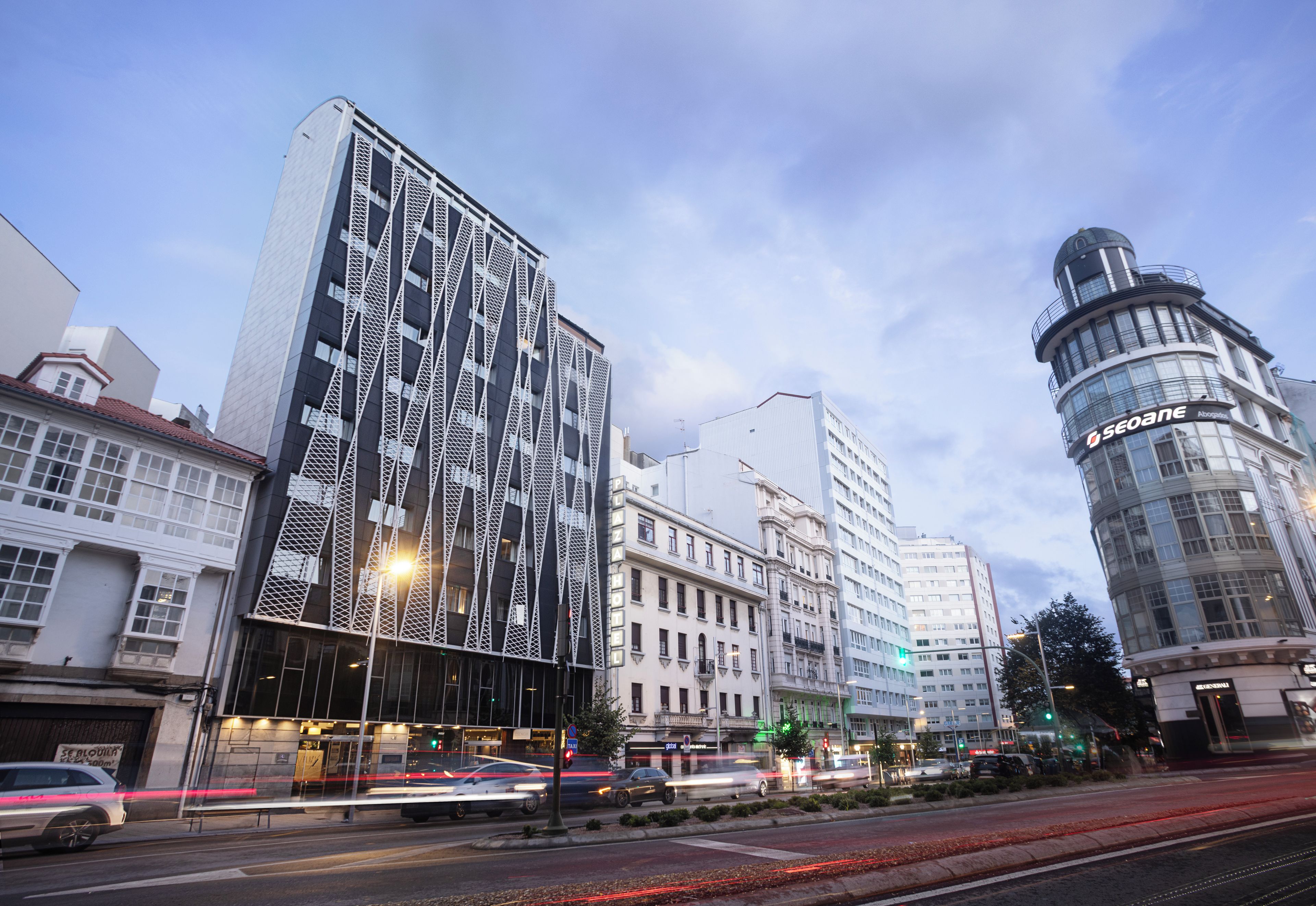 Un edificio moderno con una fachada distintiva, un edificio clásico con cúpula y una calle concurrida con vehículos en movimiento.