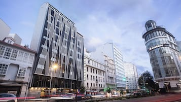 Un edificio moderno con una fachada distintiva, un edificio clásico con cúpula y una calle concurrida con vehículos en movimiento.