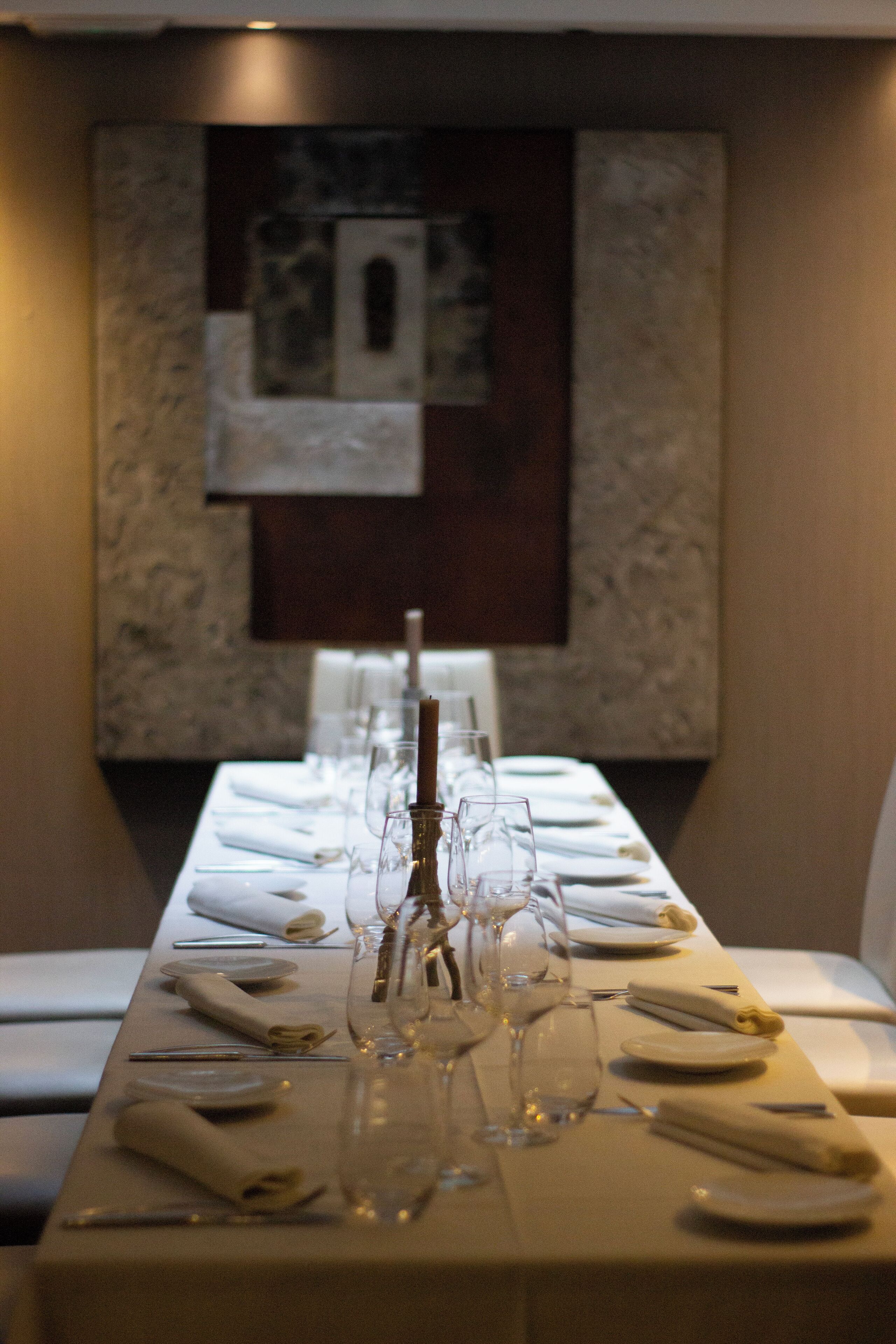 Una larga mesa de comedor dispuesta con mantel blanco, platos, vasos y un centro de mesa con velas.