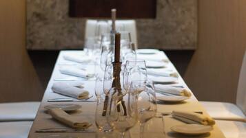 Una larga mesa de comedor dispuesta con mantel blanco, platos, vasos y un centro de mesa con velas.
