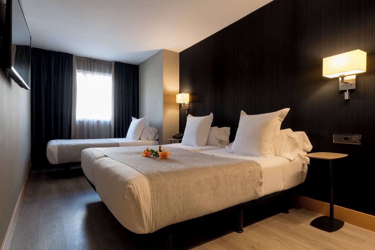 A hotel room with two beds, a flat-screen TV, a bedside table, and a lamp.