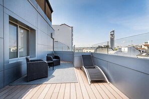 Una terraza en la azotea con piso de madera, dos sillas de mimbre, una mesa y un sillón de sol.