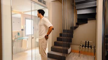 Un hombre está de pie en un interior moderno con una escalera y una puerta de cristal que da a un baño.