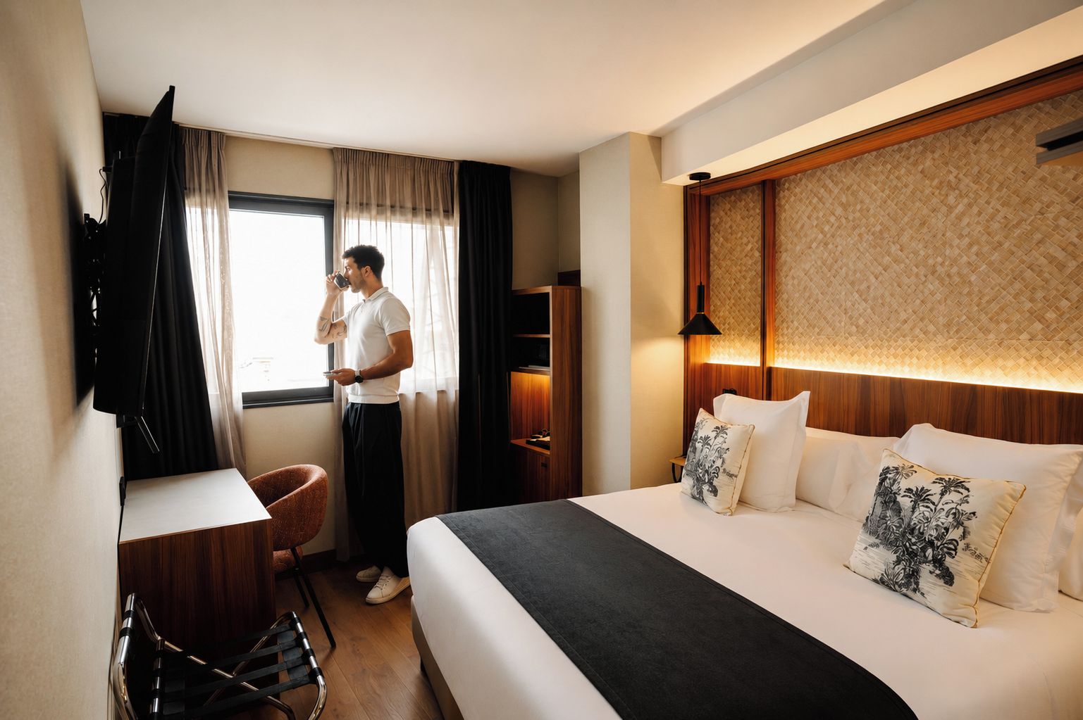 A hotel room with a bed, a desk, a chair, a TV, and a window with curtains.
