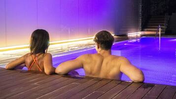 Two people sitting at the edge of a pool with a purple-lit water feature in the background.
