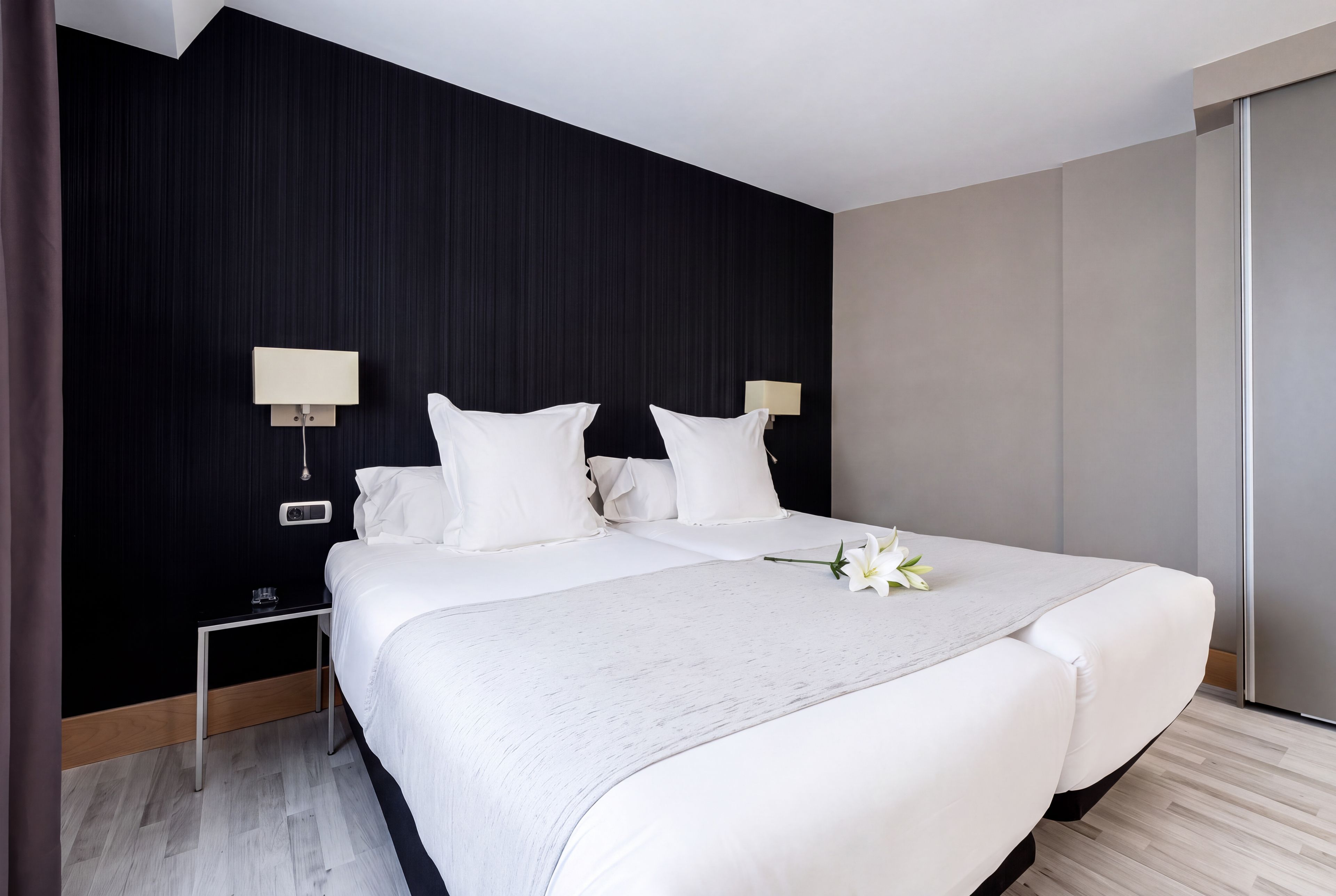 A hotel room with a large bed, two bedside lamps, a nightstand, and a wooden floor.