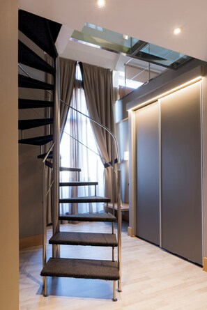 A modern interior with a glass staircase leading to a second floor, a large wardrobe, and a view through a window with curtains. - Hotel Plaza Coruña (A Coruña)